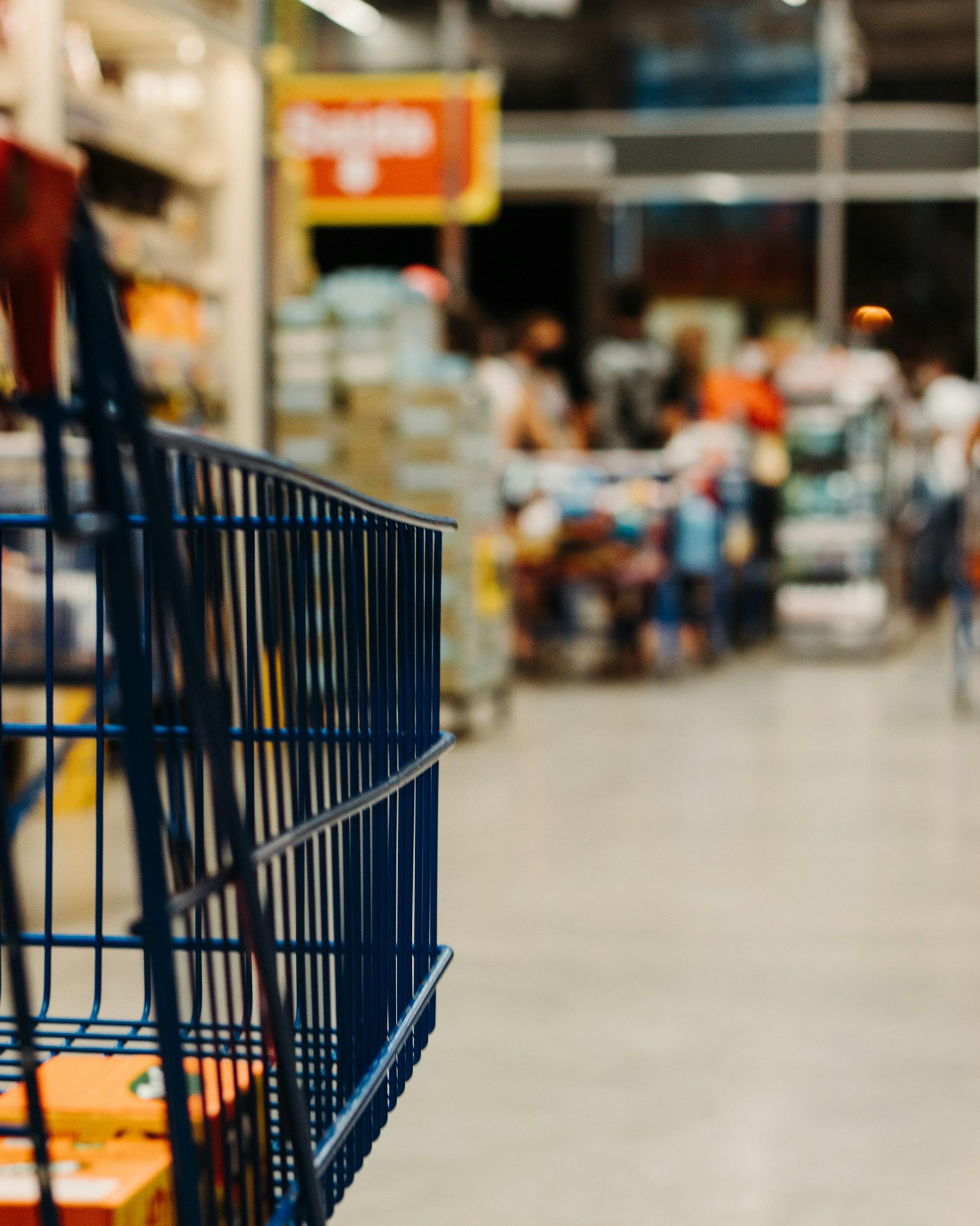 Shopping cart in a retail aisle with shoppers in the background