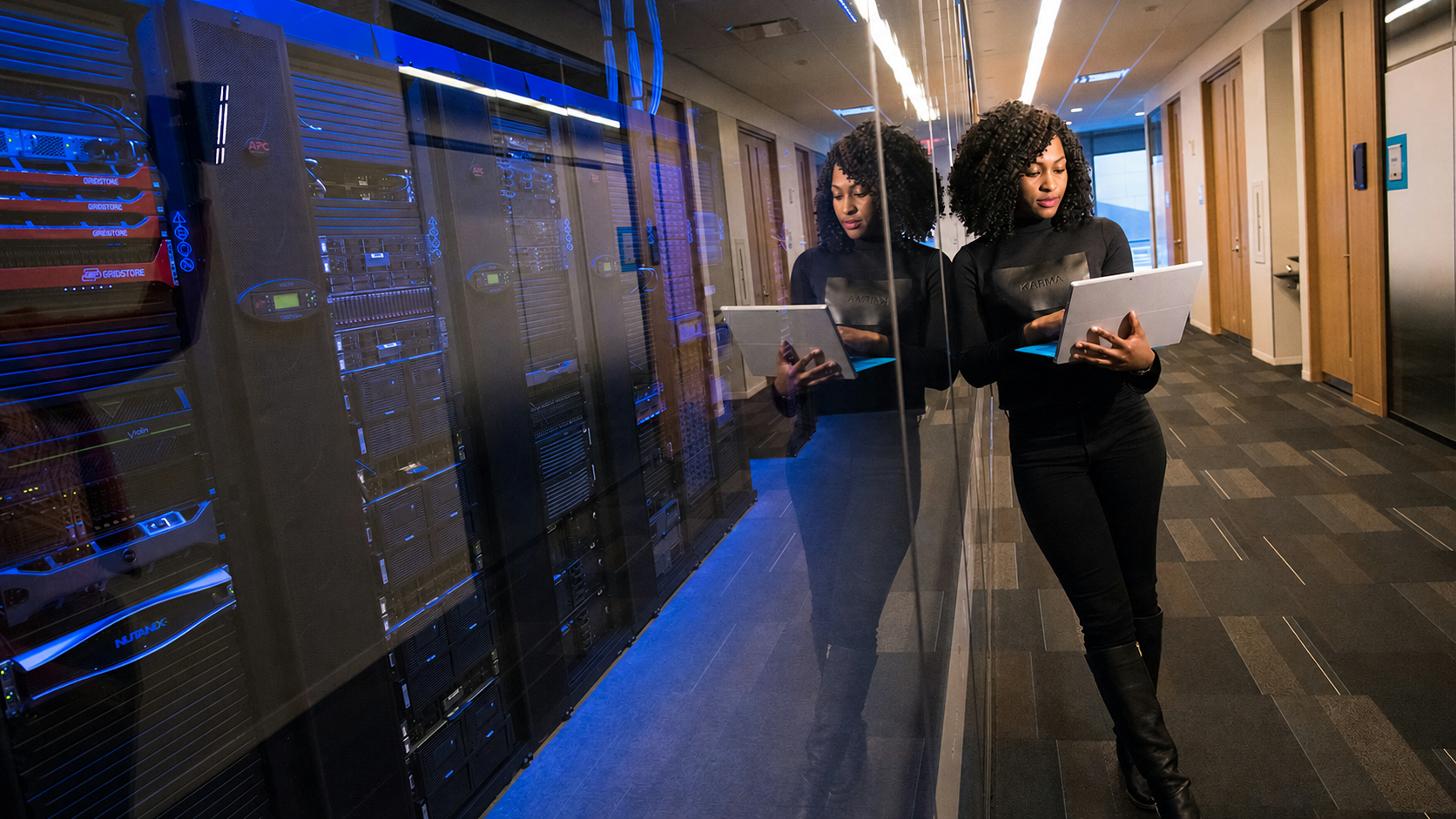 Data center corridor with server racks and a team member reviewing a tablet
